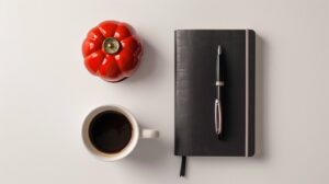 Minimalistisches Flatlay mit Bullet Journal, Espresso und roter Tomaten-Küchenuhr als Symbol der Pomodoro Variante.